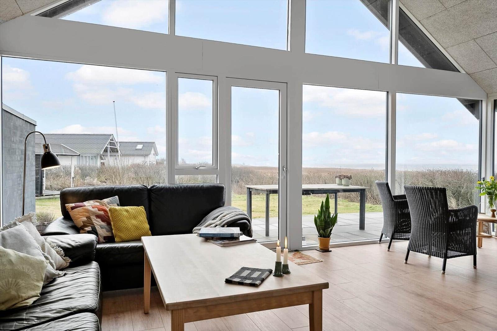 Wohnzimmer mit großem Fensterblick auf Landschaft und Terrasse mit Gartenmöbeln.