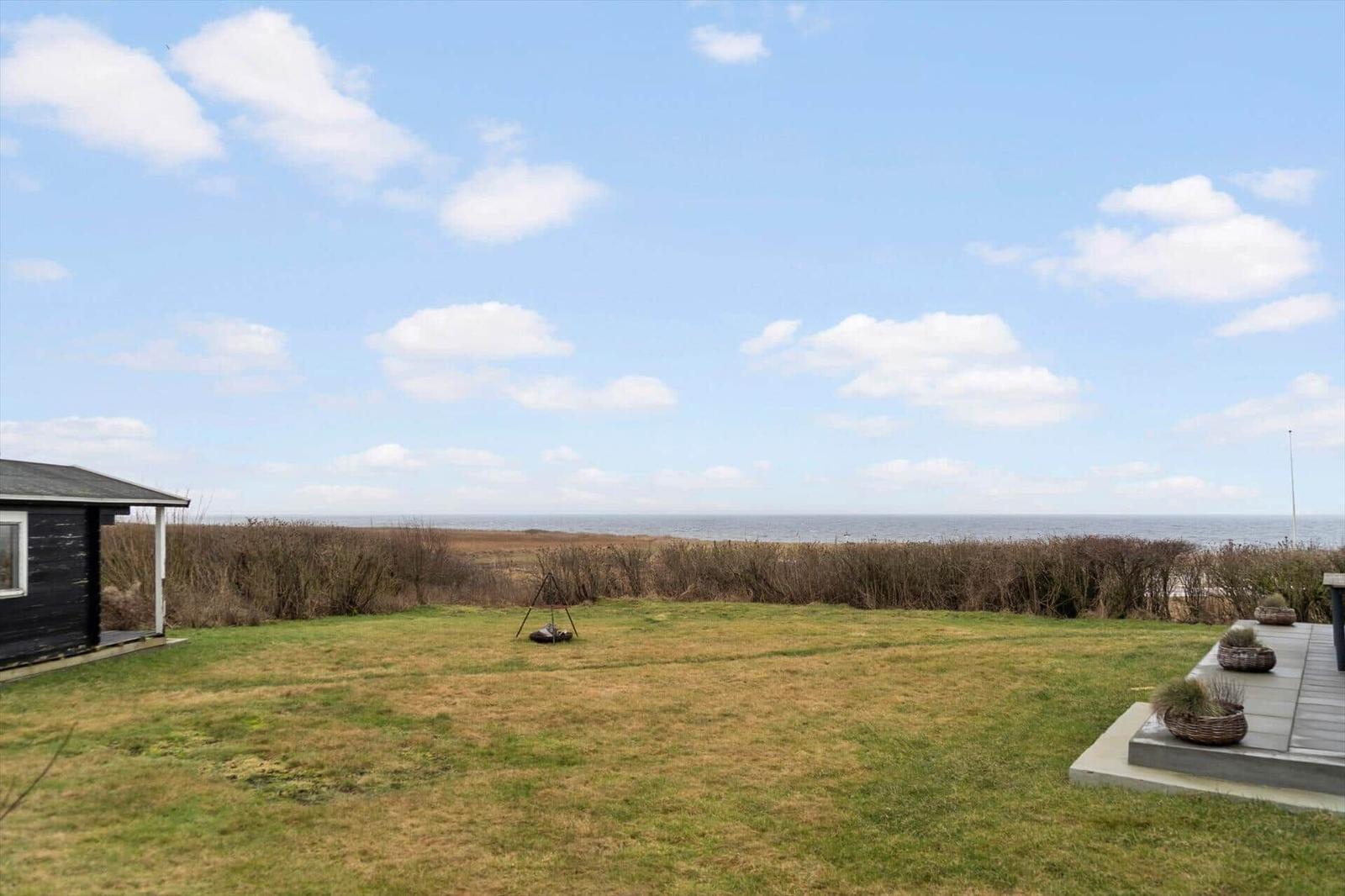 Hinterhof mit Grasfläche, Blick aufs Meer und Holzhaus mit Terrasse.