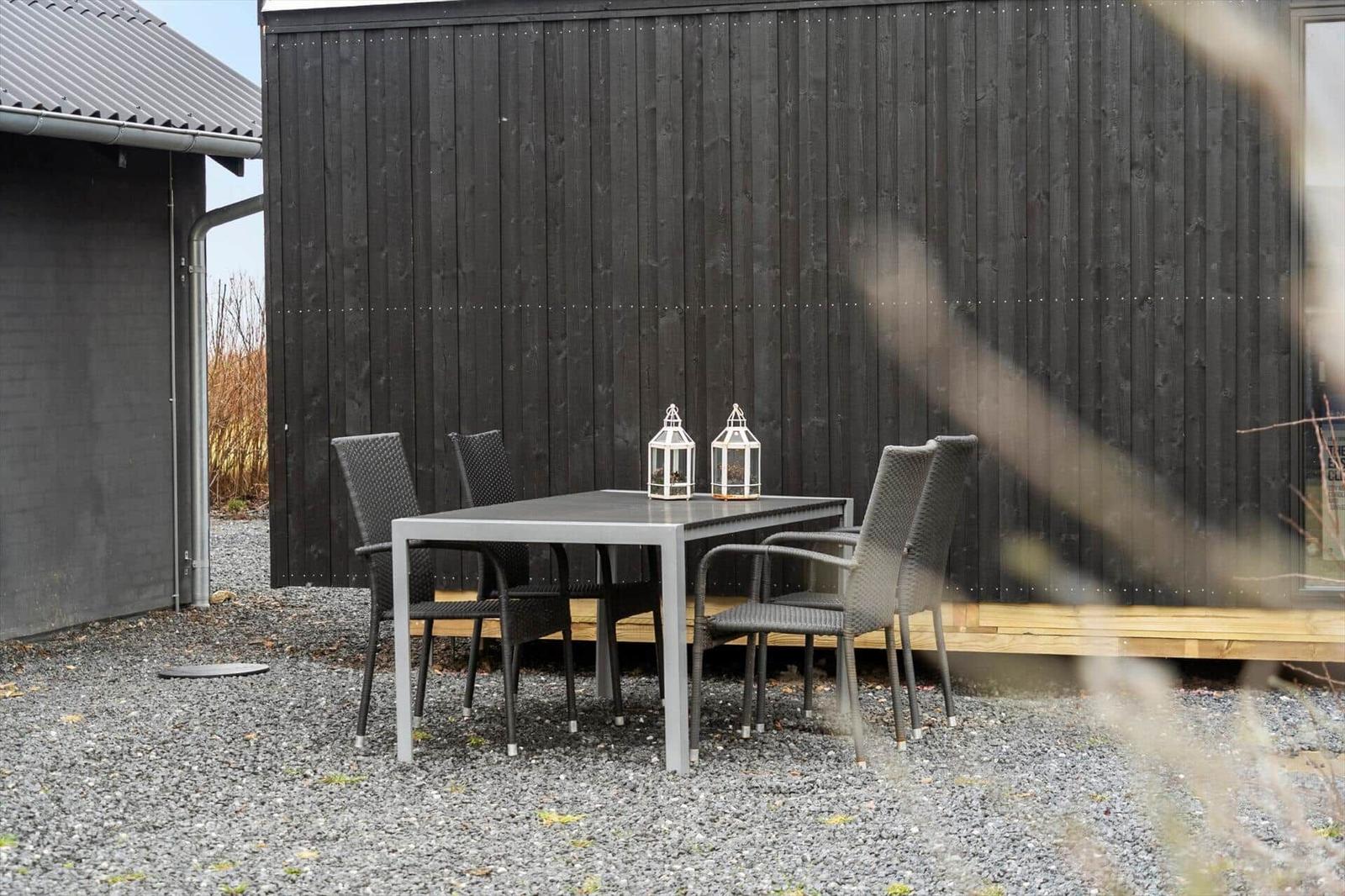 Außenbereich mit Tisch und Stühlen vor dunklem Holzhaus