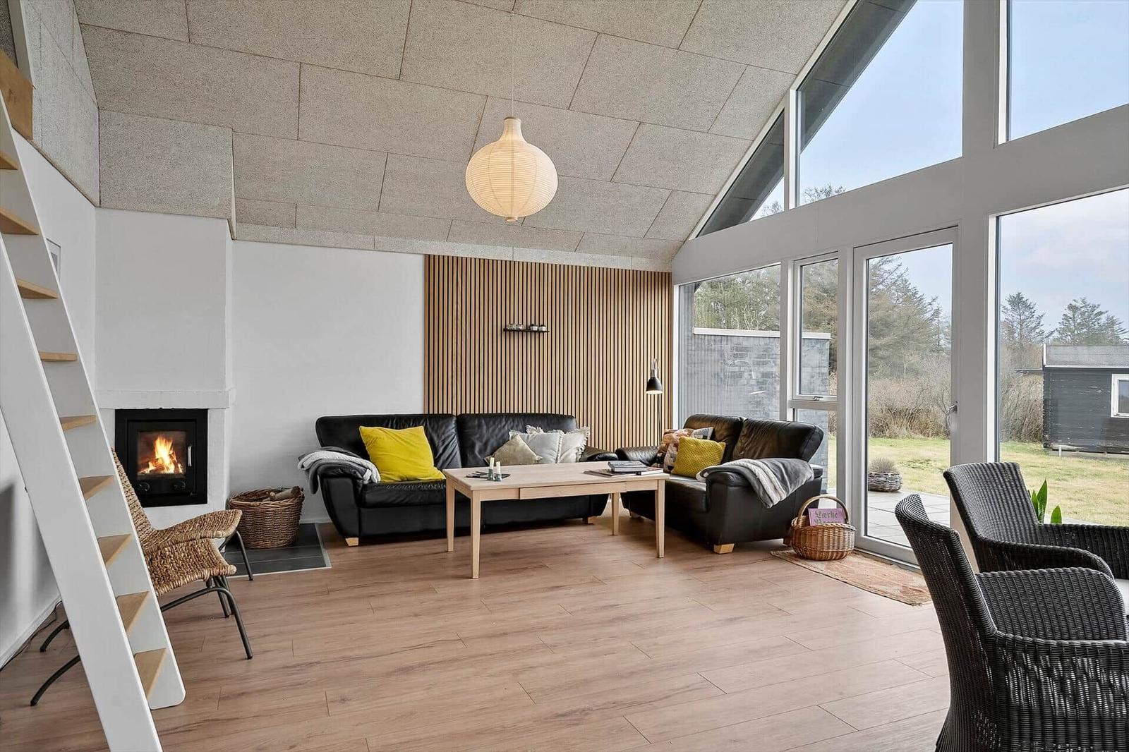 Wohnzimmer mit Sofa, Kamin und großen Fenstern.