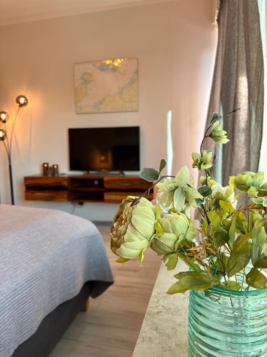 Schlafzimmer mit Bett, Fernseher und Blumen im Vordergrund.