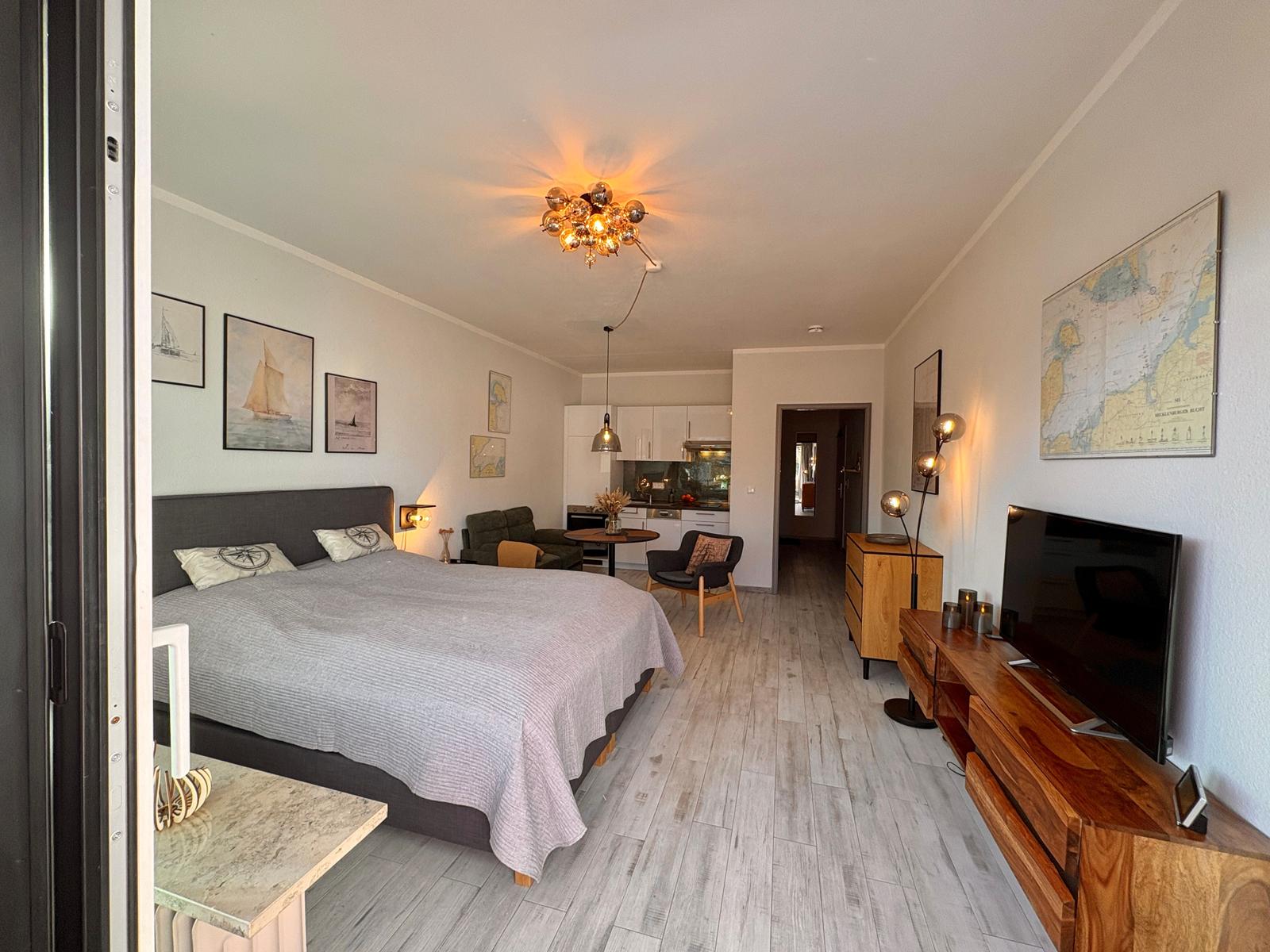 Schlafzimmer mit Bett, Wohnbereich und Küche im Hintergrund.