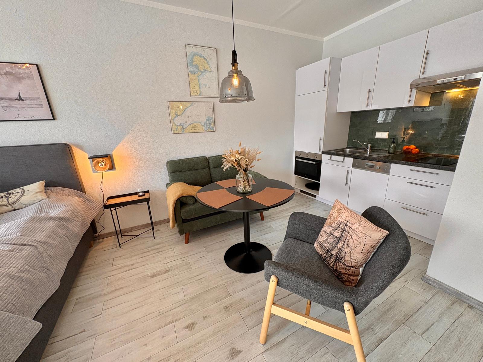 Wohnbereich mit Schlafsofa, Esstisch und Küche. Wandbilder und Pendelleuchte.