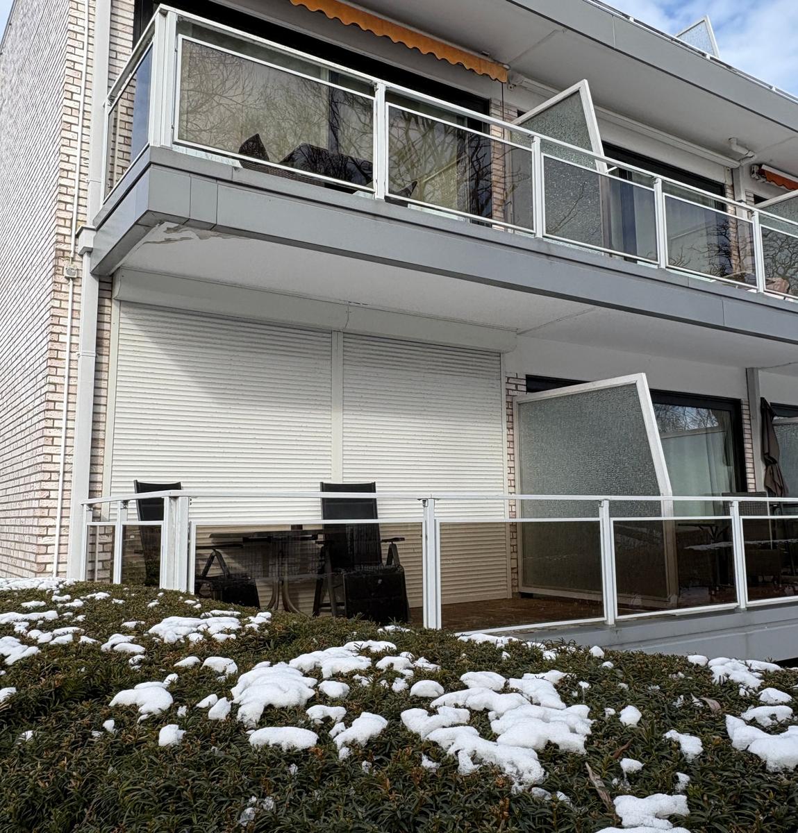 Terrasse mit Tisch und Stühlen, Schnee auf Sträuchern, Balkon mit Glasgeländer