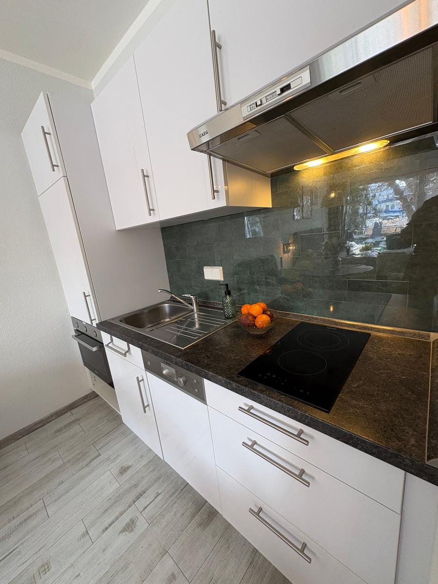 Küche mit weißen Schränken, dunklem Arbeitsplatz und Edelstahlspüle.