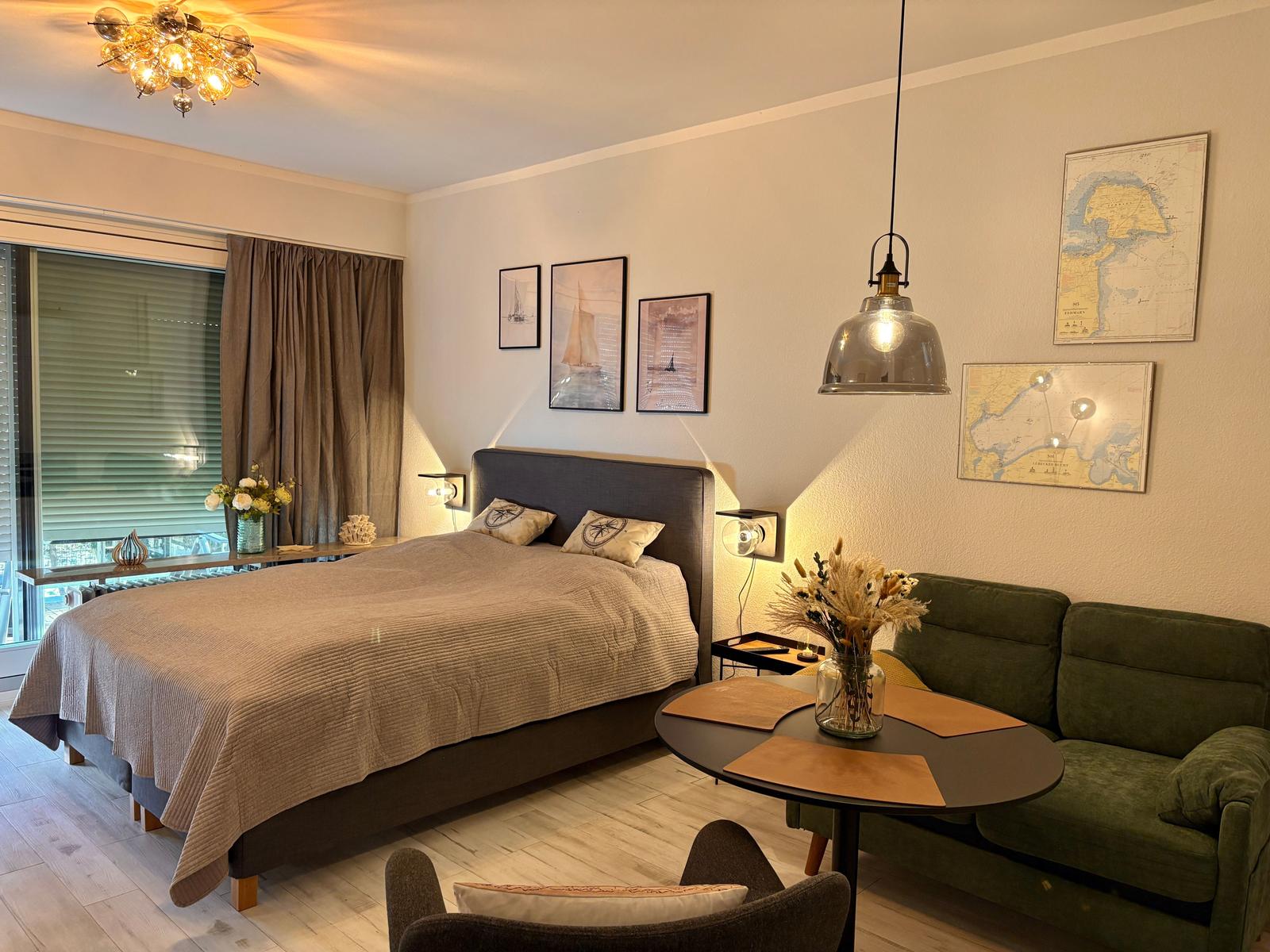 Schlafzimmer mit Bett, Sofa und Tisch. Wanddekoration und Fenster mit Jalousien.