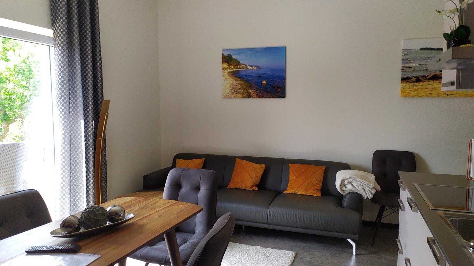 Wohn- und Essbereich mit Sofa, Tisch und Küchenzeile. An der Wand hängen zwei Bilder.