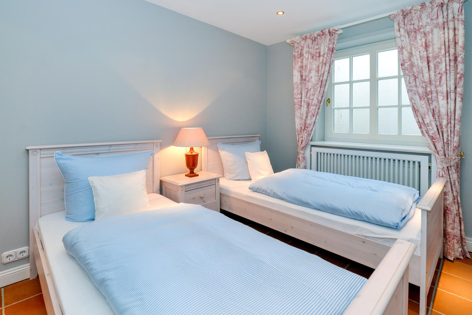 Zwei Betten mit blauen Bettwäsche, Nachttisch und Fenster mit Vorhängen.