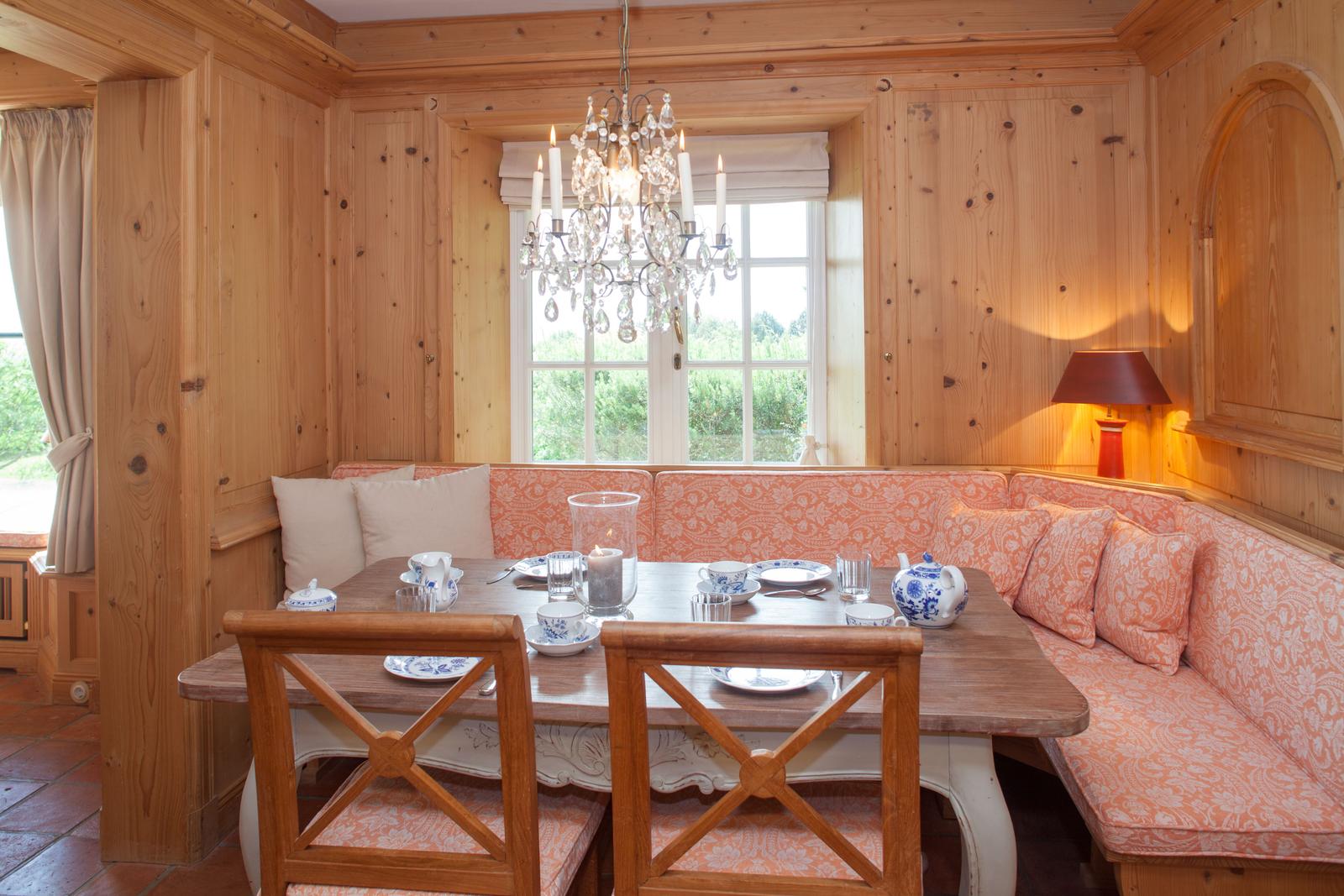 Esszimmer mit Holzwand, Bank mit orangefarbenem Stoff und Tisch mit Geschirr.