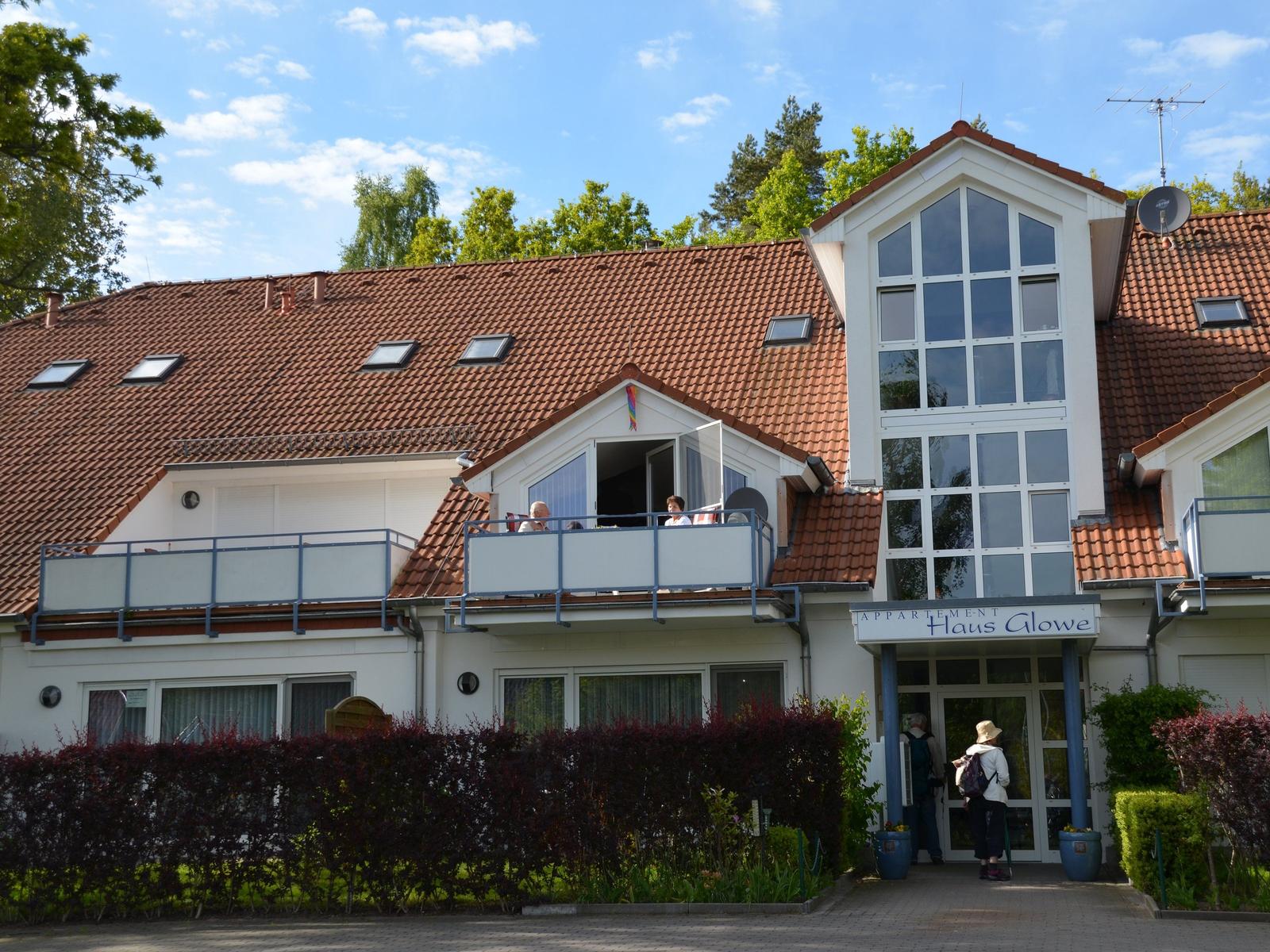 Appartementhaus mit Balkon und rotem Dach unter blauem Himmel.