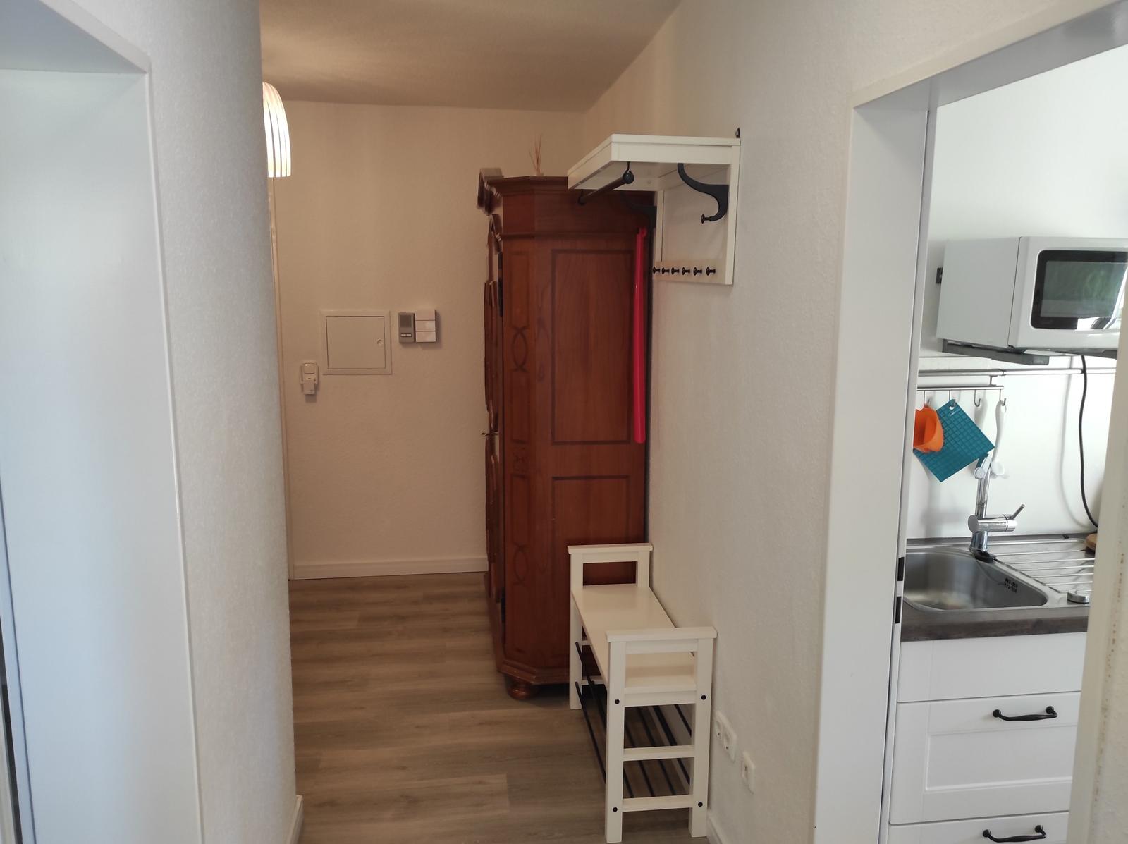 Flur mit Kleiderschrank, Stuhl und Blick in die Küche.