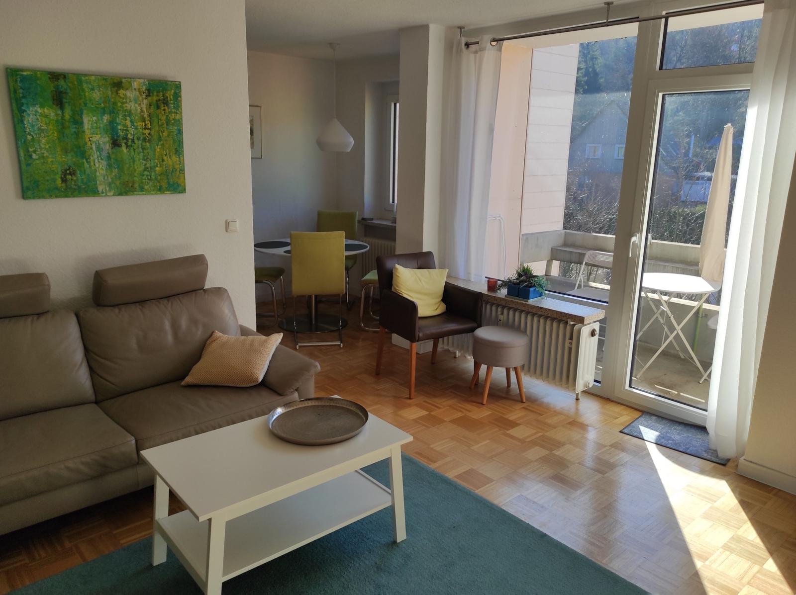 Wohnzimmer mit Sofa, Couchtisch und Balkon. Holzboden und große Fenster.