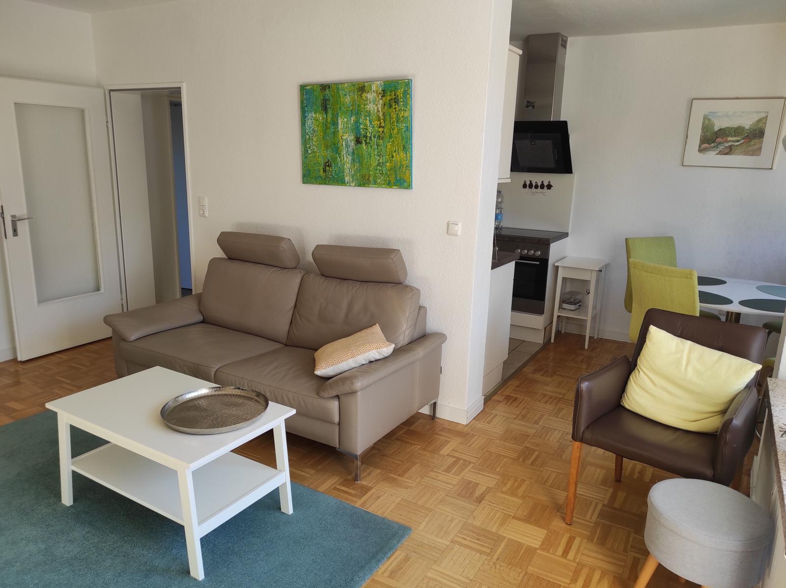 Wohnzimmer mit Sofa, Sessel und Essbereich. Holzfußboden und Wandbild.