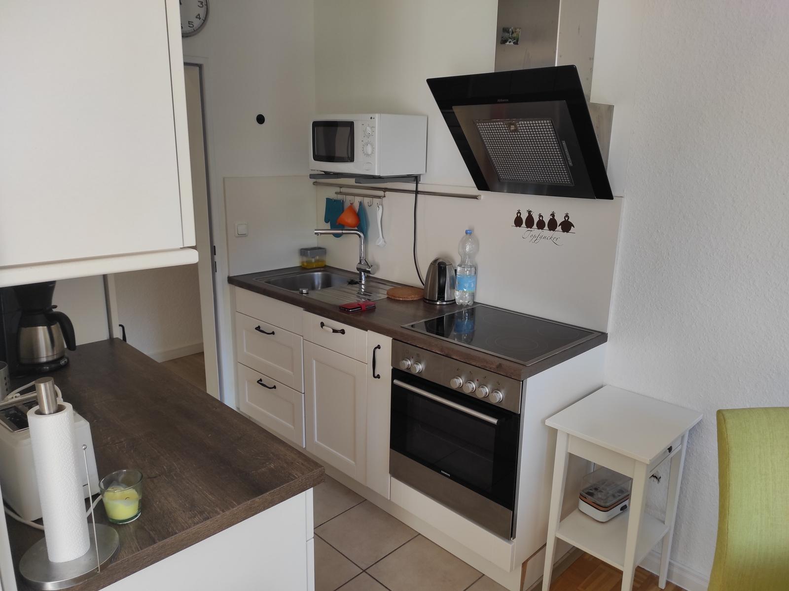 Küche mit Herd, Dunstabzug, Spüle und Mikrowelle.