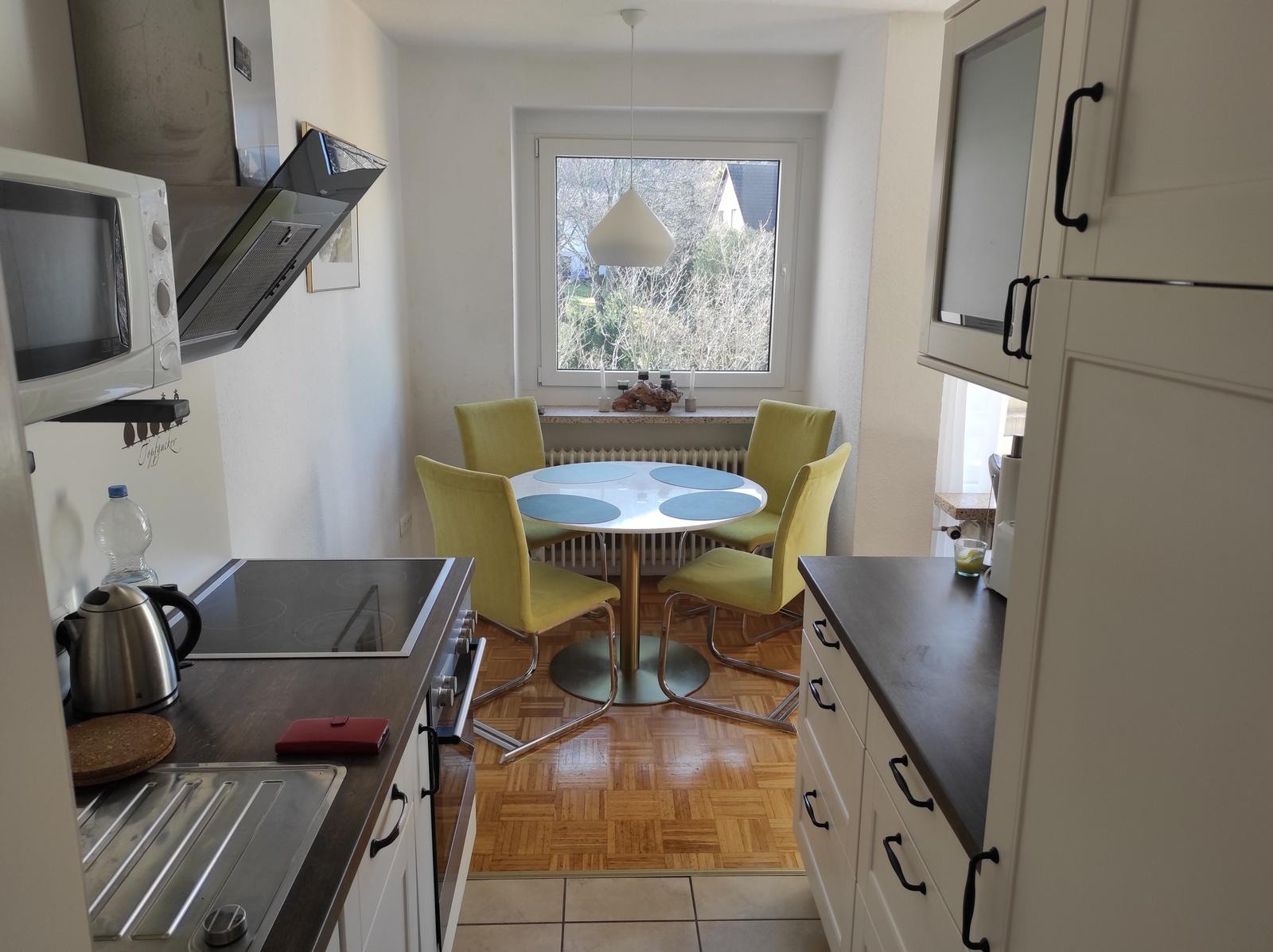 Küche mit Essbereich, runden Tisch und gelben Stühlen. Fenster mit Blick auf Garten.