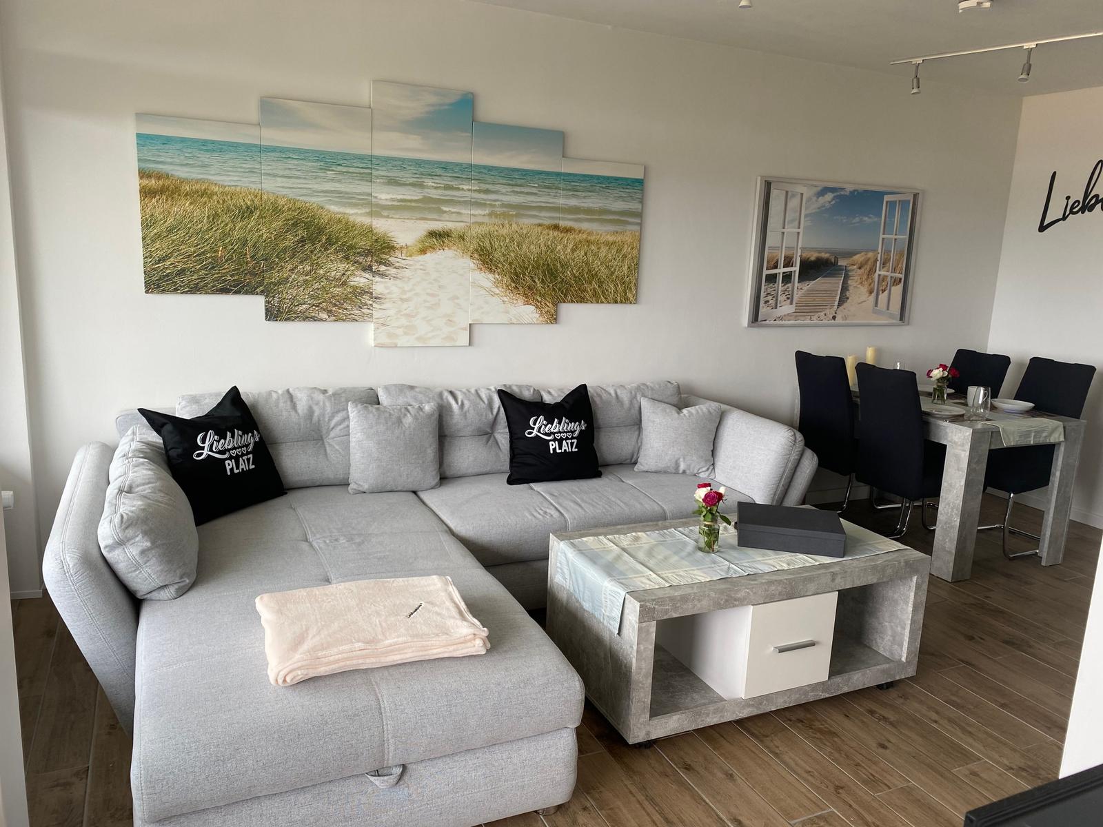 Großer Wohnbereich mit Sofa, Esstisch und Strandmotiven an den Wänden.