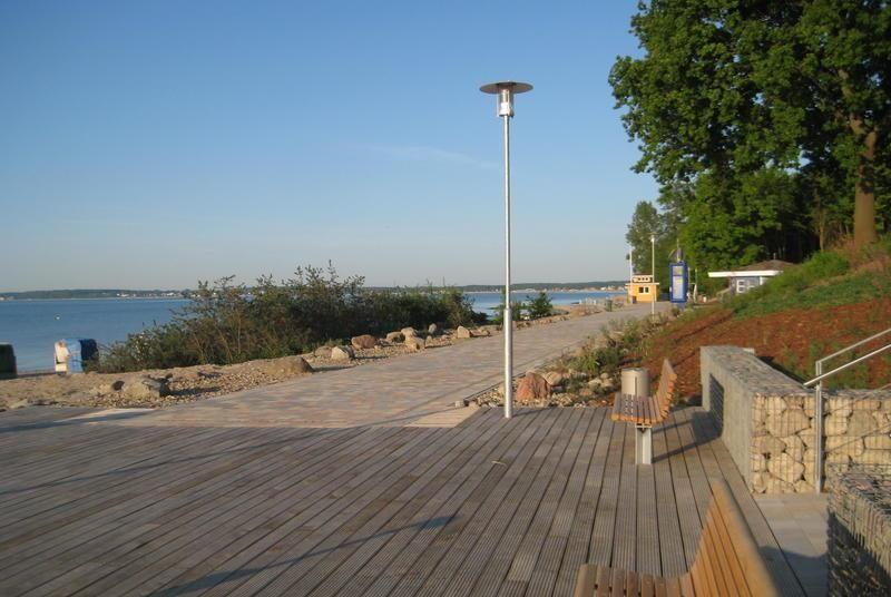 Holzterrasse mit Blick auf Wasser und Bäume. Bank und Laterne sind sichtbar.