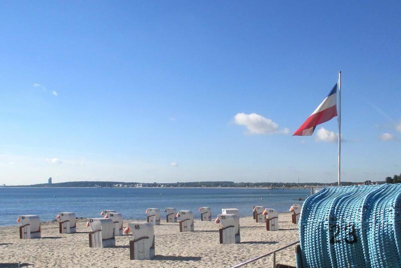 Strand mit Strandkörben und französischer Flagge am Horizont.