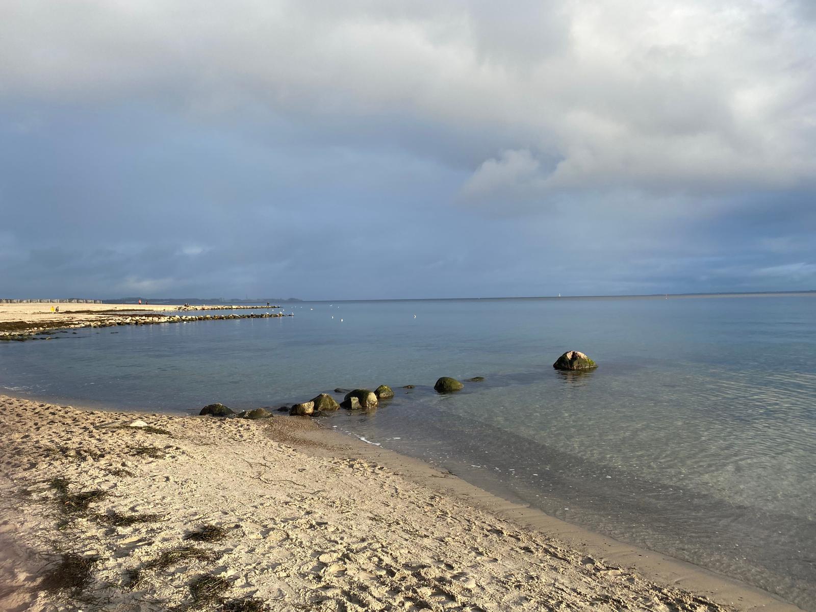 Strand mit Steinen und ruhigem Wasser unter bewölktem Himmel
