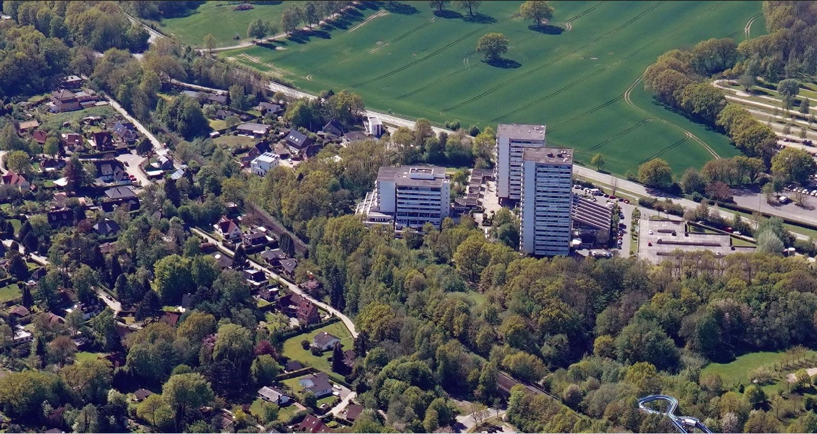 Luftbild von Wohngebieten und Hochhäusern umgeben von grünen Feldern und Bäumen.