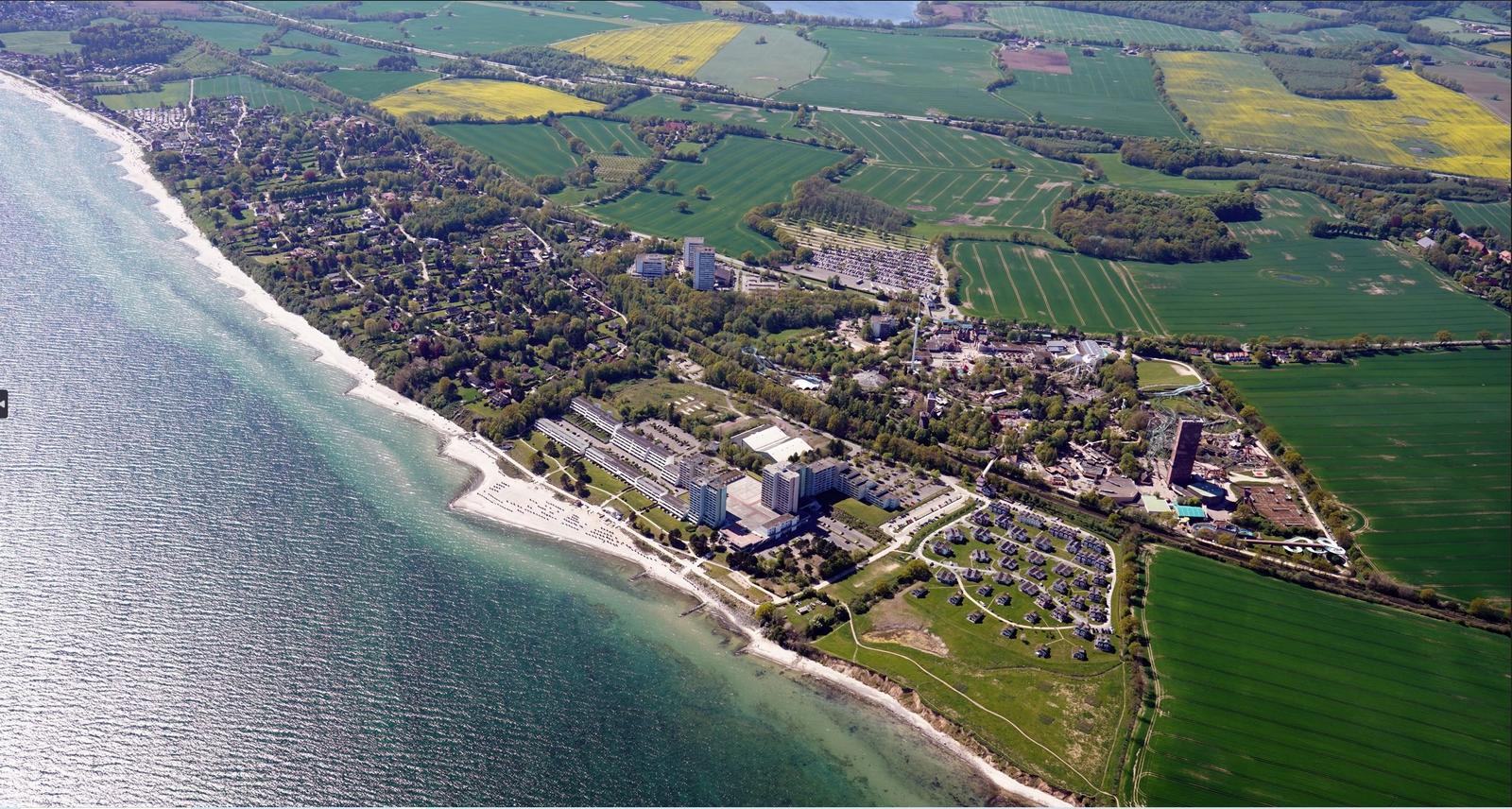 Aerial view of coastal town with beach, hotels, and green fields.