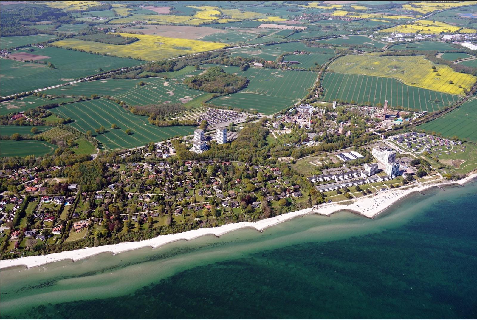 Aerial view of coastal area with beach, green fields, and buildings.