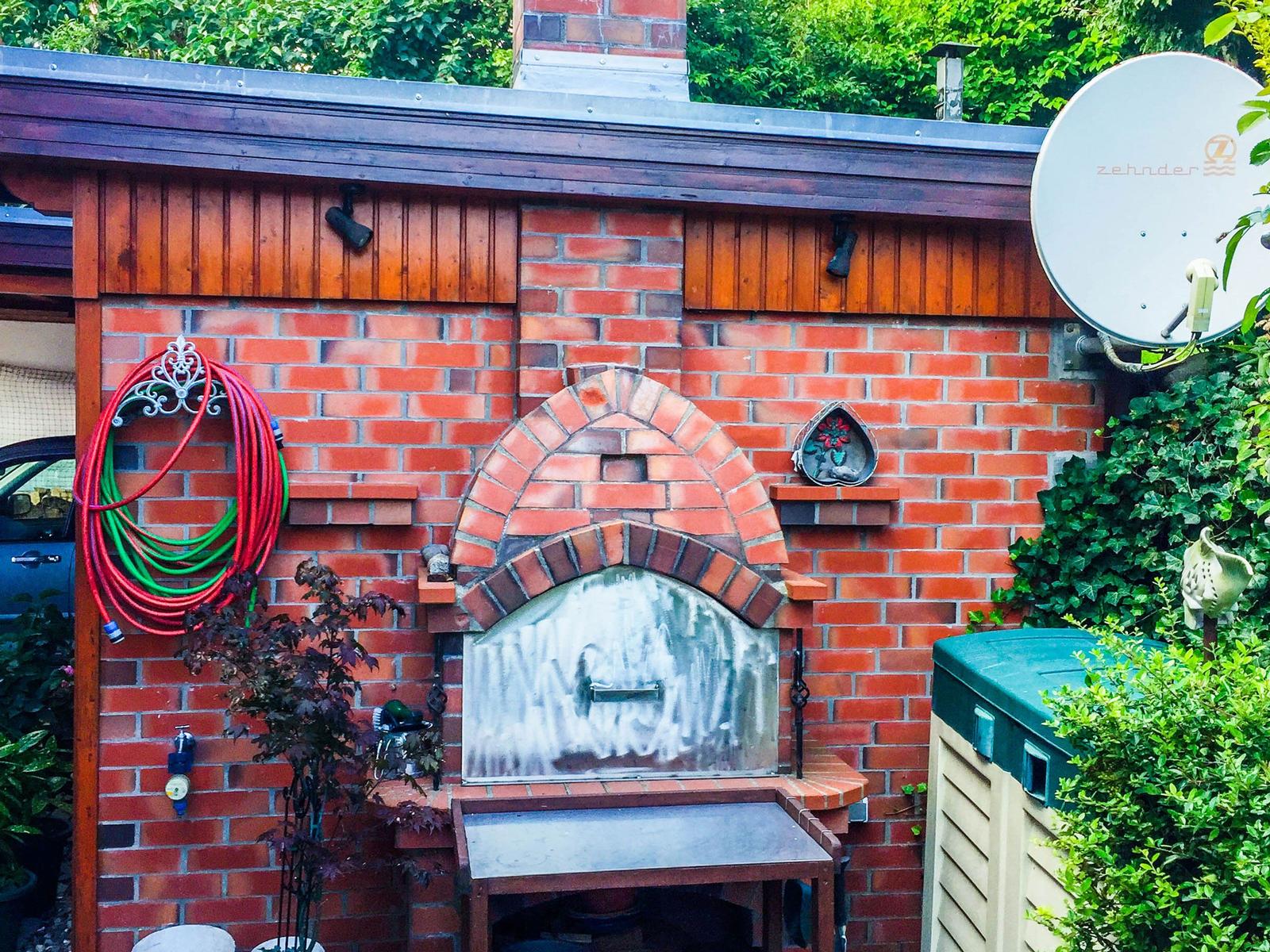Außenbereich mit Backofen, Schlauch und Satellitenschüssel an Backsteinwand
