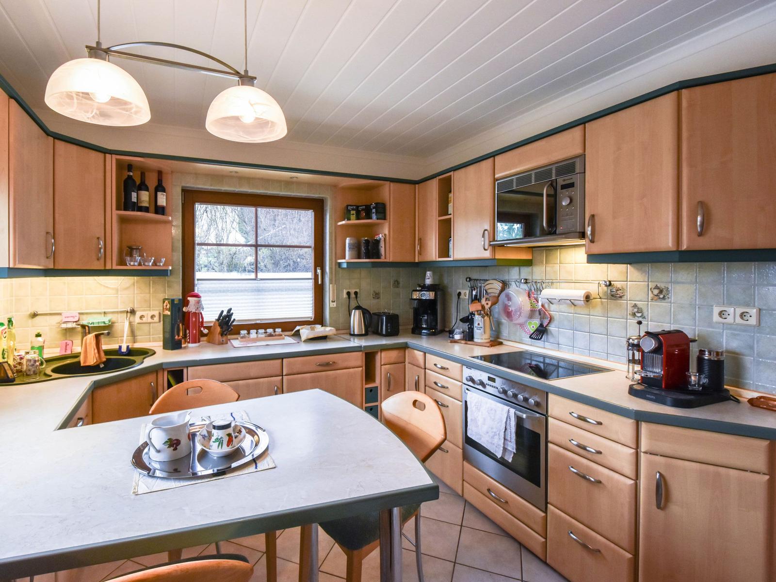 Küche mit Holzschränken, Arbeitsplatte und Fenster zum Außenbereich.