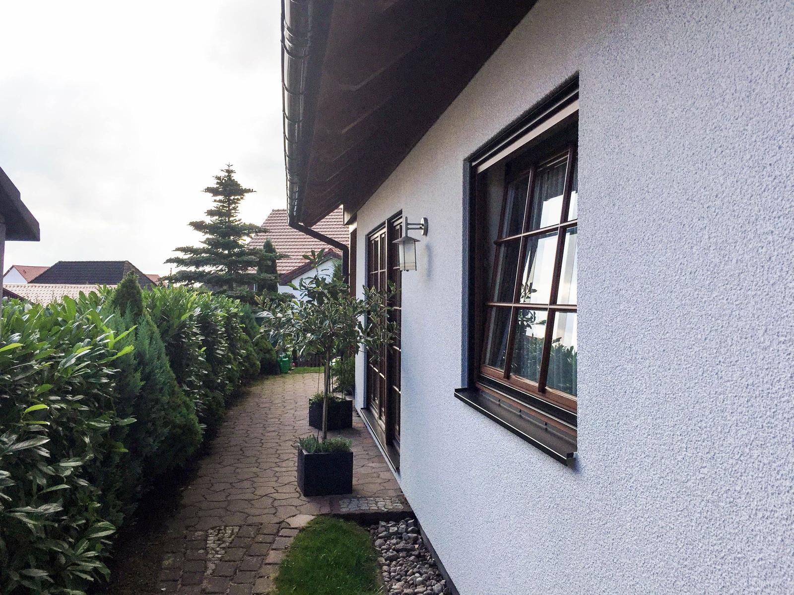 Haus mit gepflasterter Allee, grünen Hecken und Fenstern mit Holzrahmen.