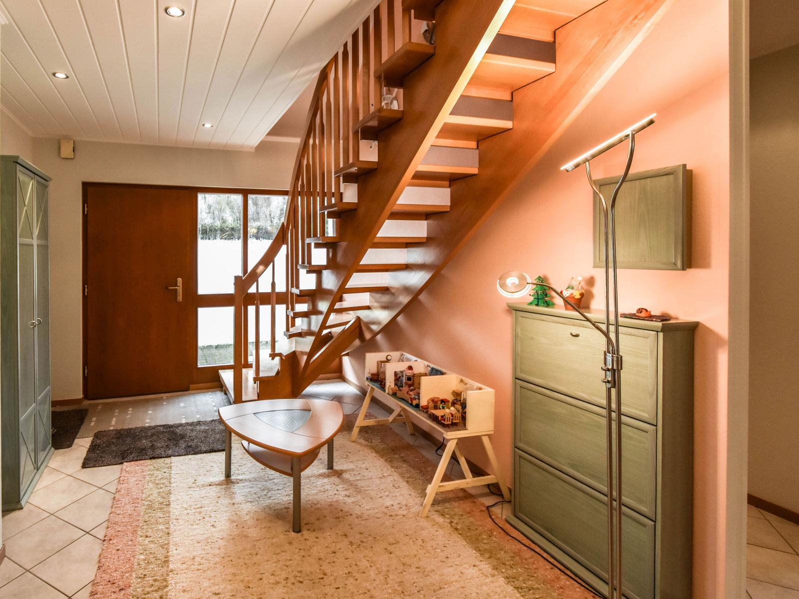 Eingangsbereich mit Holztreppe, Schrank und Tisch. Spielzeugregal und Stehlampe sind sichtbar.