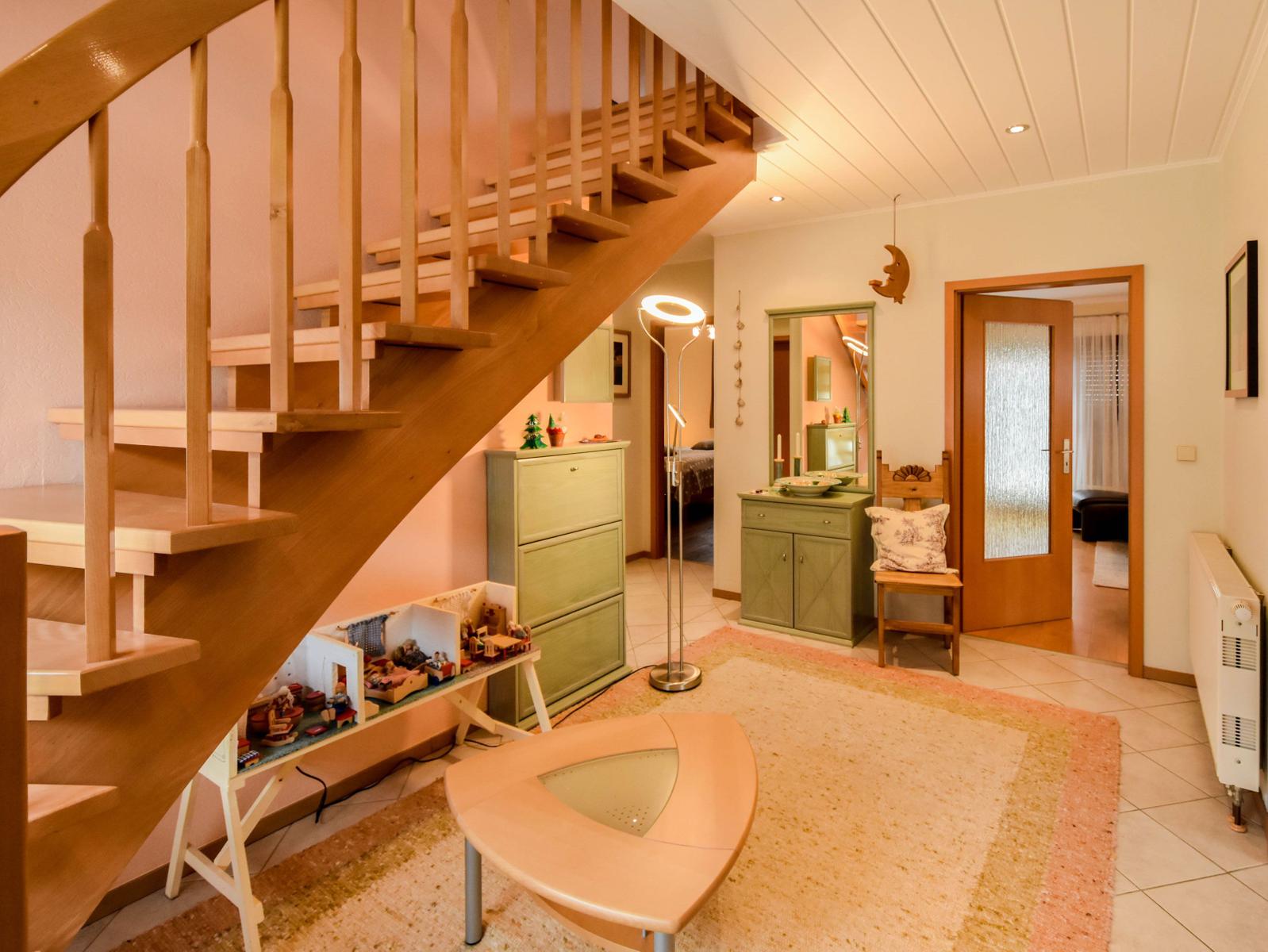 Holzstiege, grüner Schrank, Teppich und Sitzgelegenheit im Eingangsbereich.