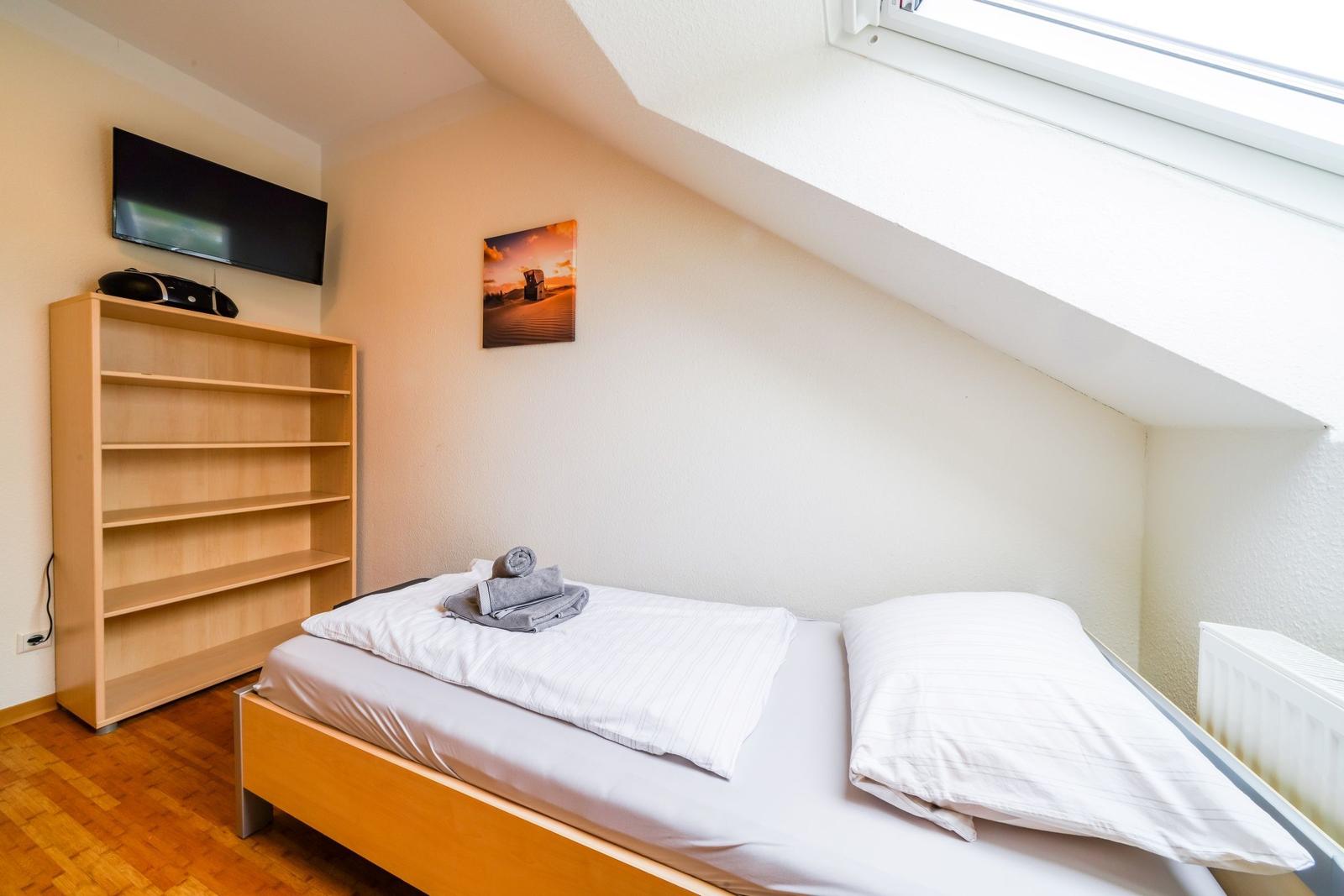 Schlafzimmer mit Dachschrägen, Bett, Fernseher und Bücherregal.