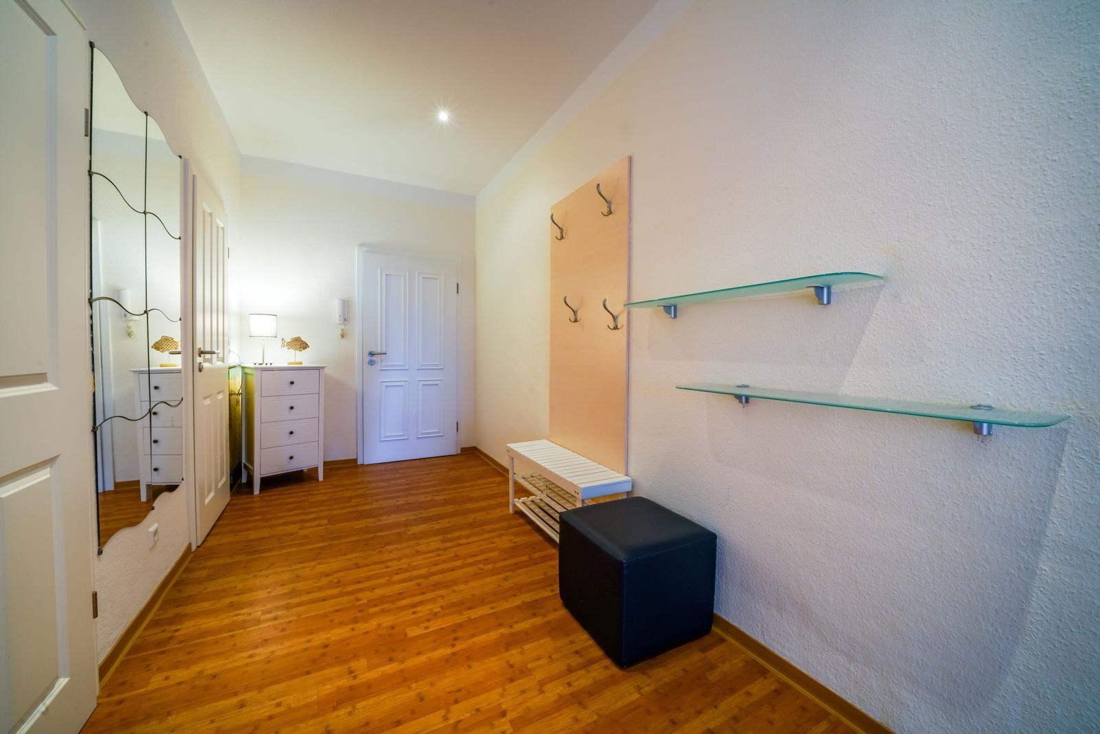 Flur mit Holzboden, Spiegel, Garderobe und Glasregalen.