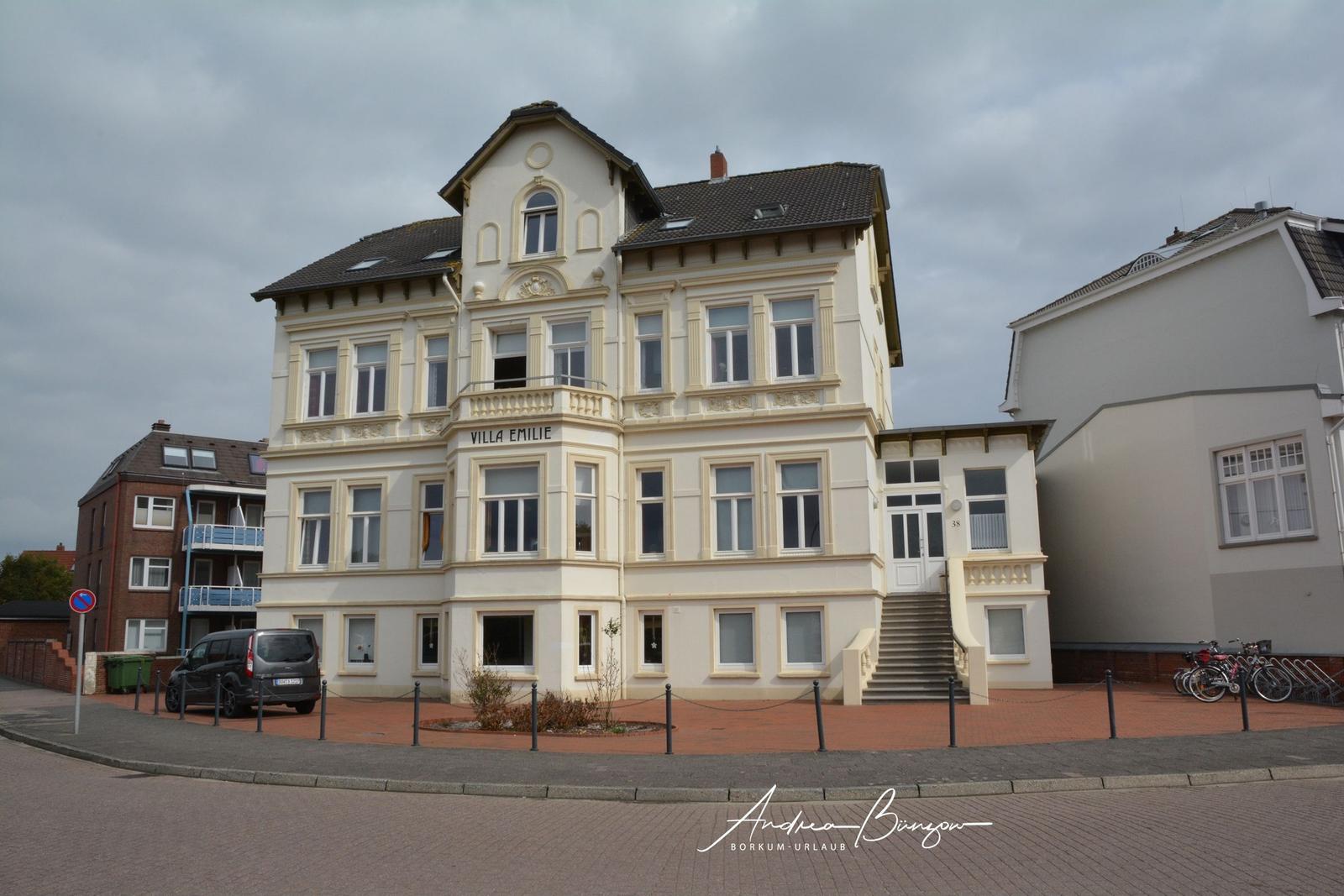 Villa Emilie mit Balkon und Eingangstreppe. Parkplatz und Fahrräder vor dem Haus.