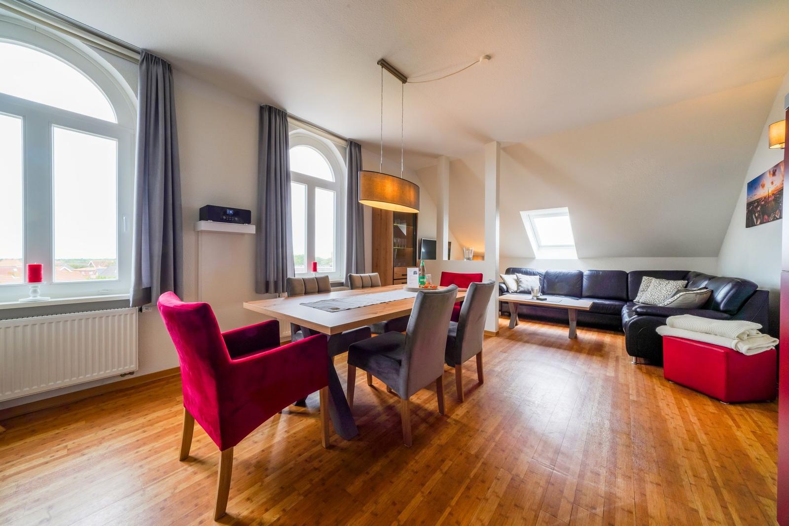 Wohn- und Essbereich mit Holzboden, Sofa, Esstisch und Fenstern.
