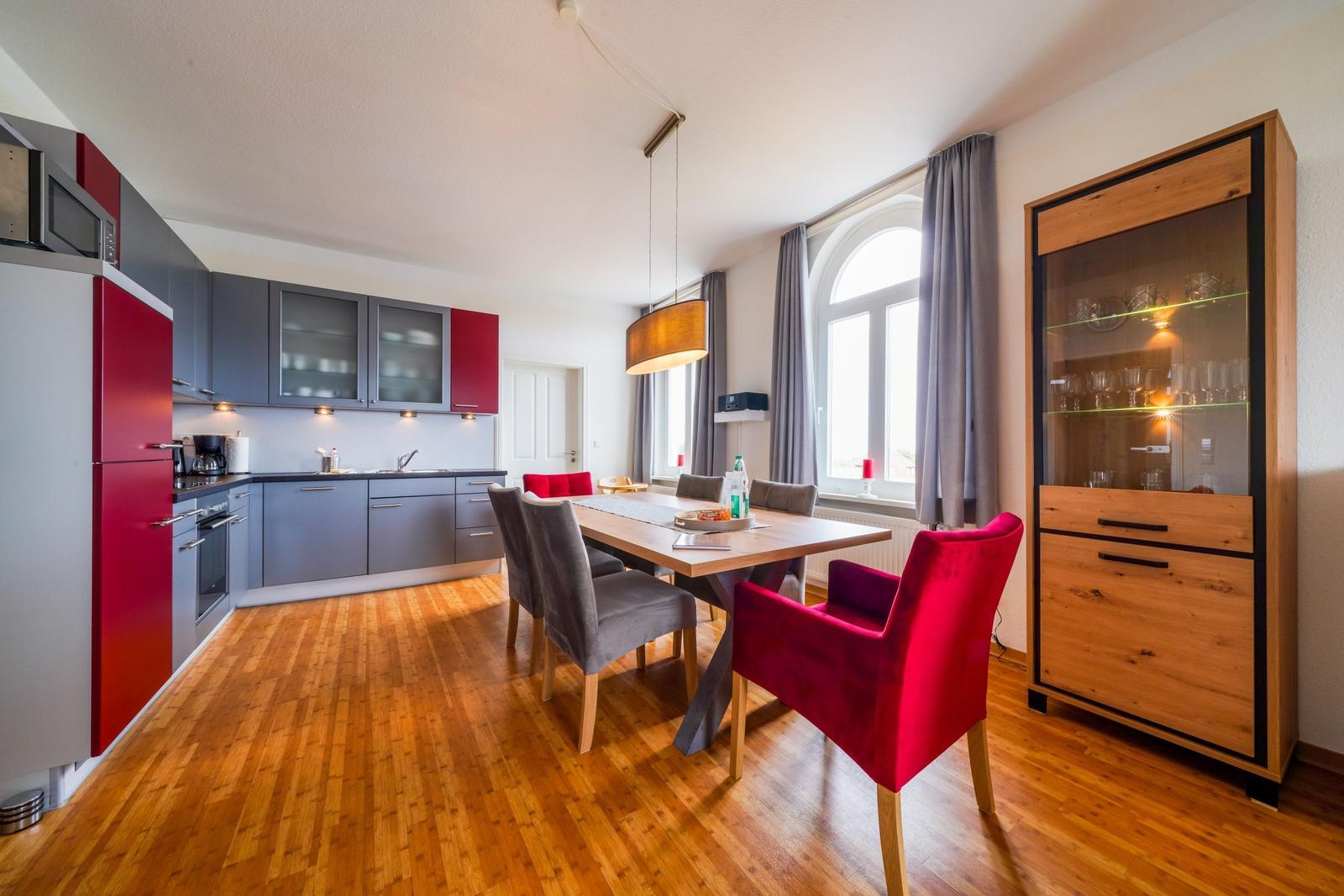 Küche und Essbereich mit Holzboden, rotem Kühlschrank und Glasvitrine.