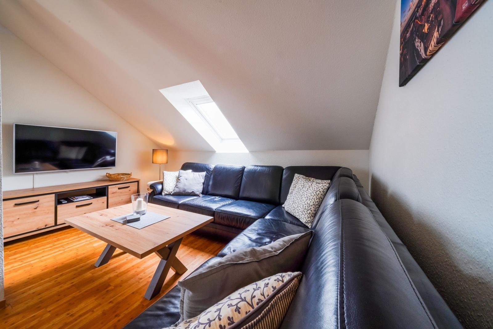 Wohnzimmer mit Sofa, Couchtisch und Fernseher unter Dachschräge