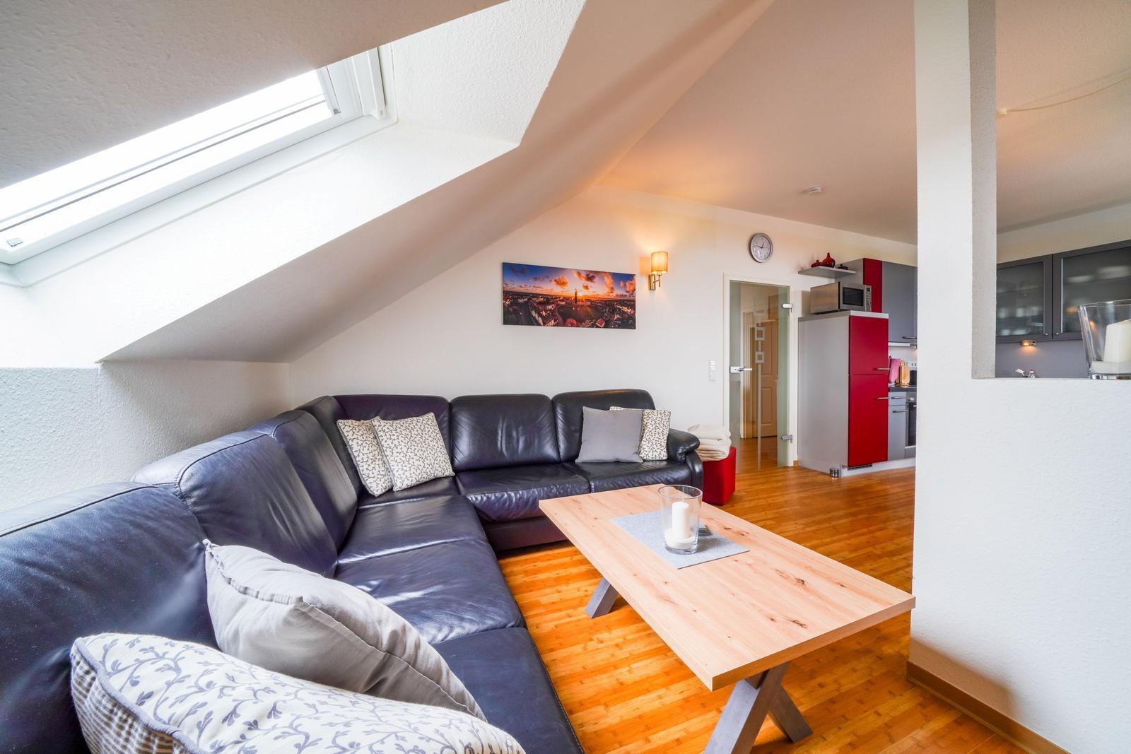 Wohnzimmer mit Sofa, Tisch und Dachfenster. Küche im Hintergrund.