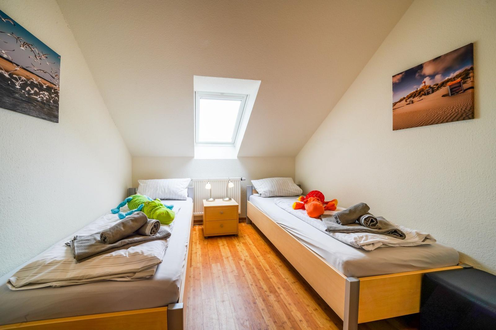 Zwei Einzelbetten unter Dachschrägen mit Fenster und Wandbildern.