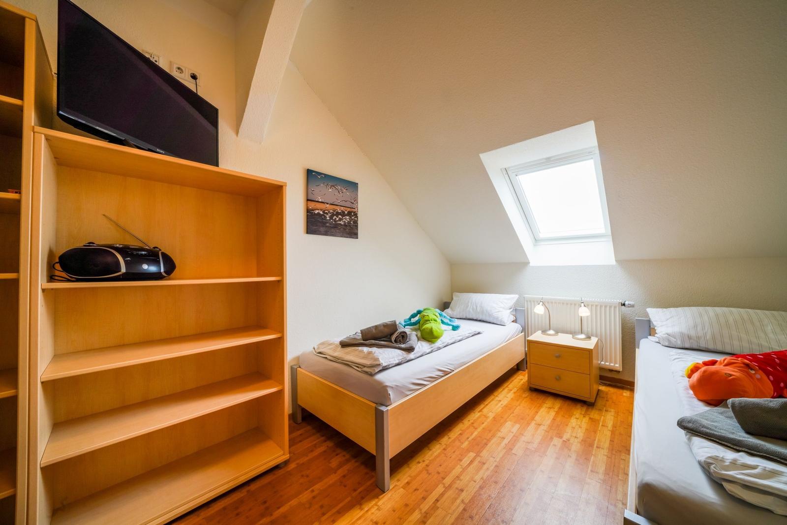 Zimmer mit zwei Betten, Dachschrägen, Dachfenster und Holzboden.