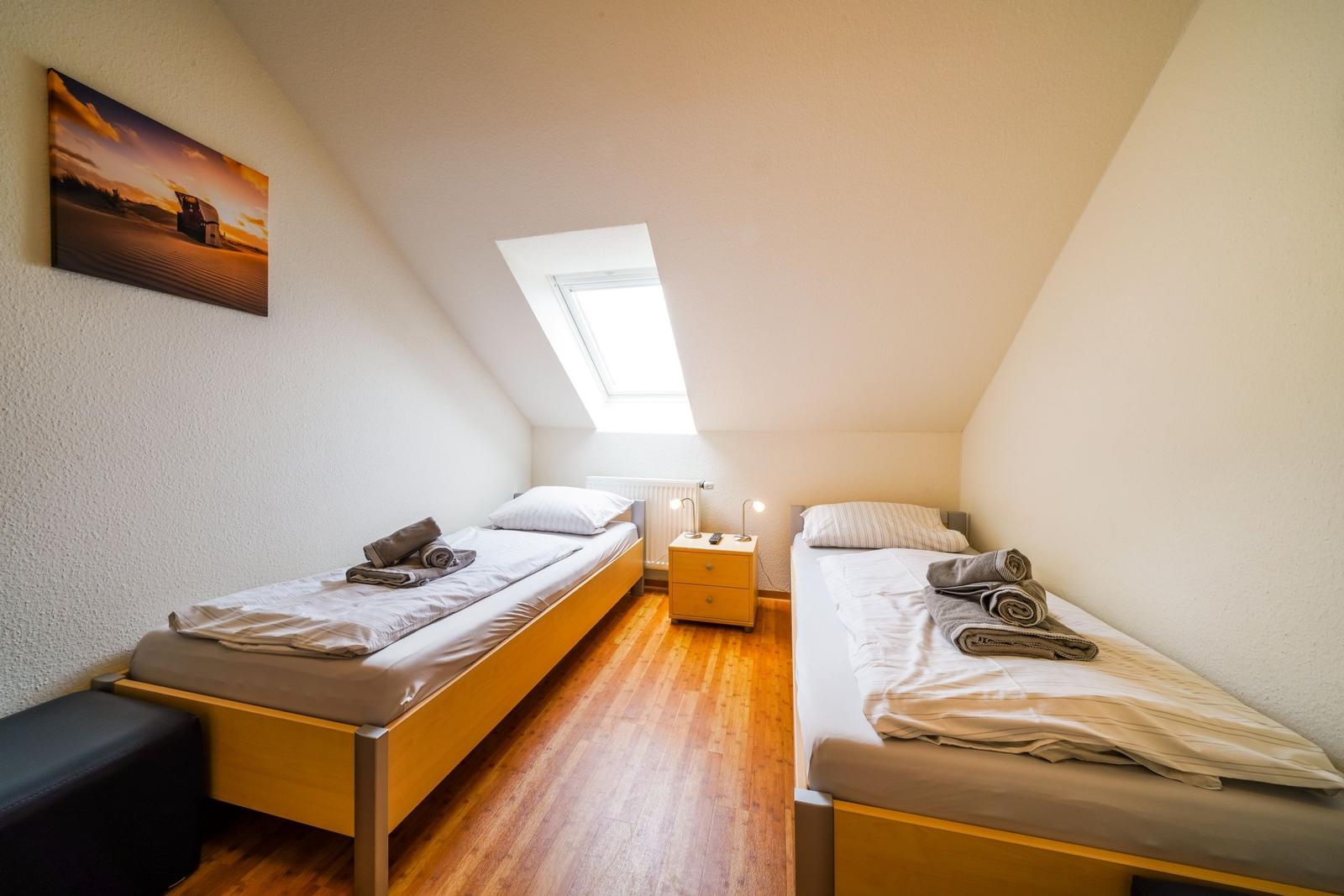 Zwei Einzelbetten, kleiner Nachttisch, Dachschräge mit Dachfenster, Wandbild, Holzboden.