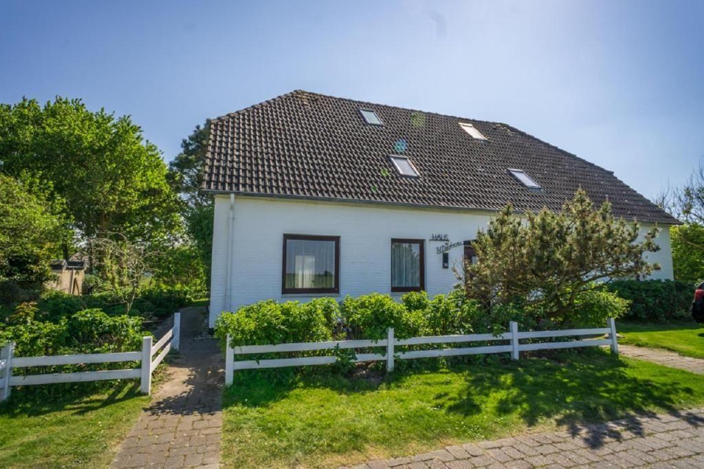 Weißes Haus mit braunem Dach, grüner Umgebung und weißem Zaun.