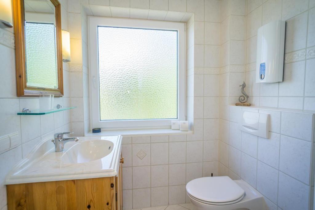 Badezimmer mit Waschbecken, Toilette und Fenster mit getöntem Glas.