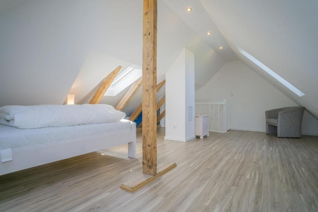 Schlafzimmer mit Dachschrägen, Holzboden und Fenster. Bett, Sitzgelegenheit und Holzstütze sichtbar.