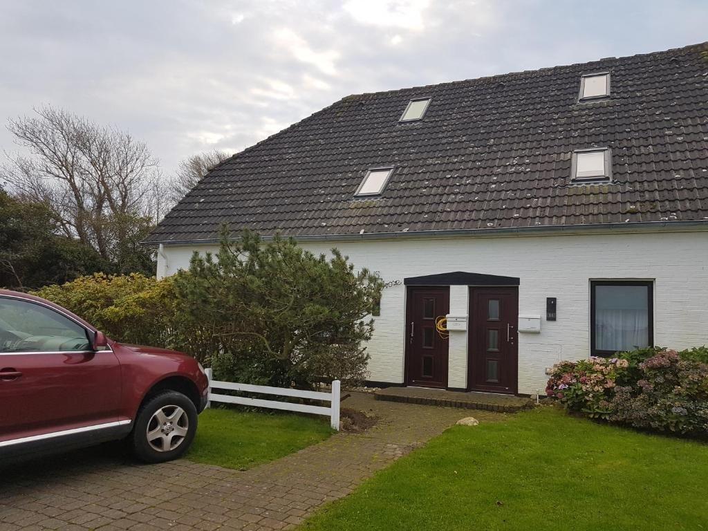 Weiße Villa mit dunklem Dach und zwei Eingangstüren. Vorgarten mit Gras und Strauch.