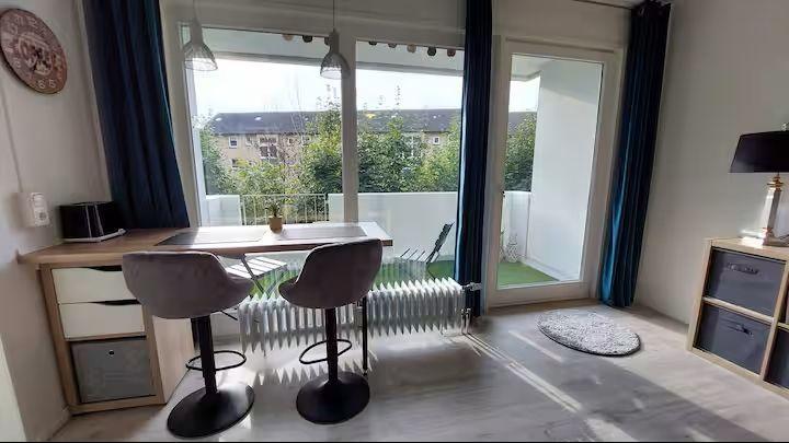 Raum mit Tisch, zwei Barhockern und Balkonansicht.