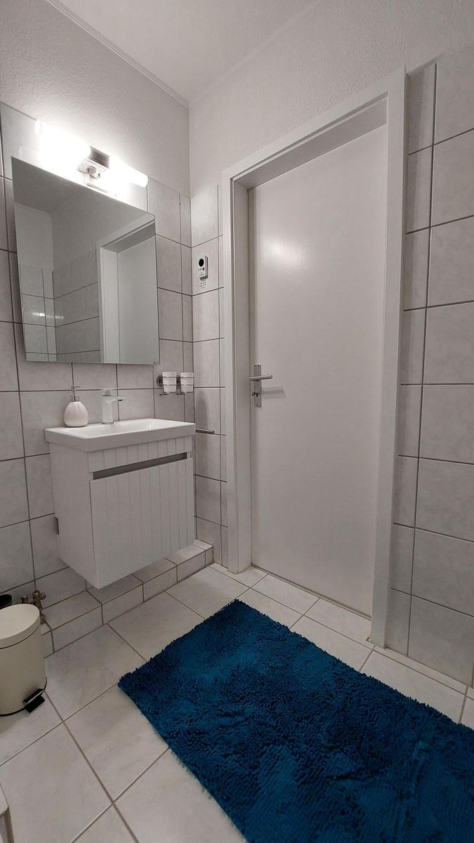 Badezimmer mit Waschbecken, Spiegel und blauem Teppich