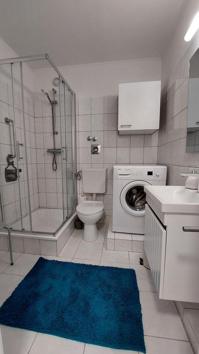 Badezimmer mit Dusche, WC, Waschmaschine und Waschtisch.