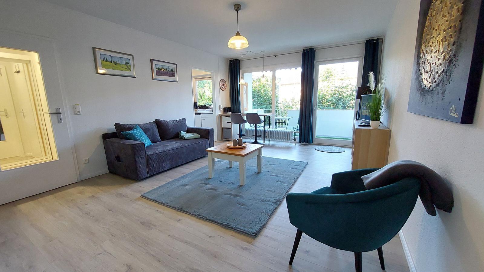 Wohnzimmer mit Sofa, Sessel und Balkon. Holzboden und Wandbilder.