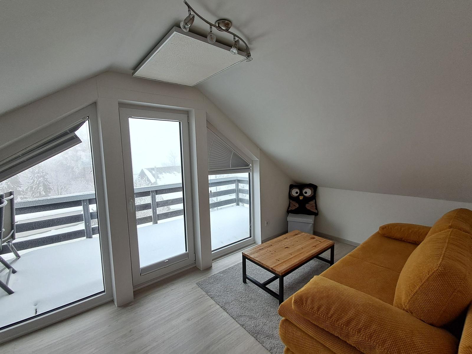 Wohnzimmer mit gelbem Sofa, Holztisch und Balkon mit Schneeansicht.